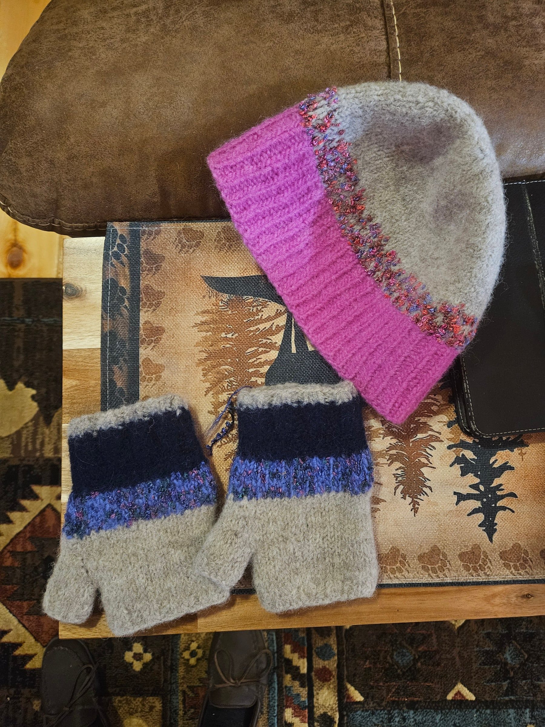 A magenta felted hat and a pair of navy-and-gray fingerless mittens resting on a patterned mat.