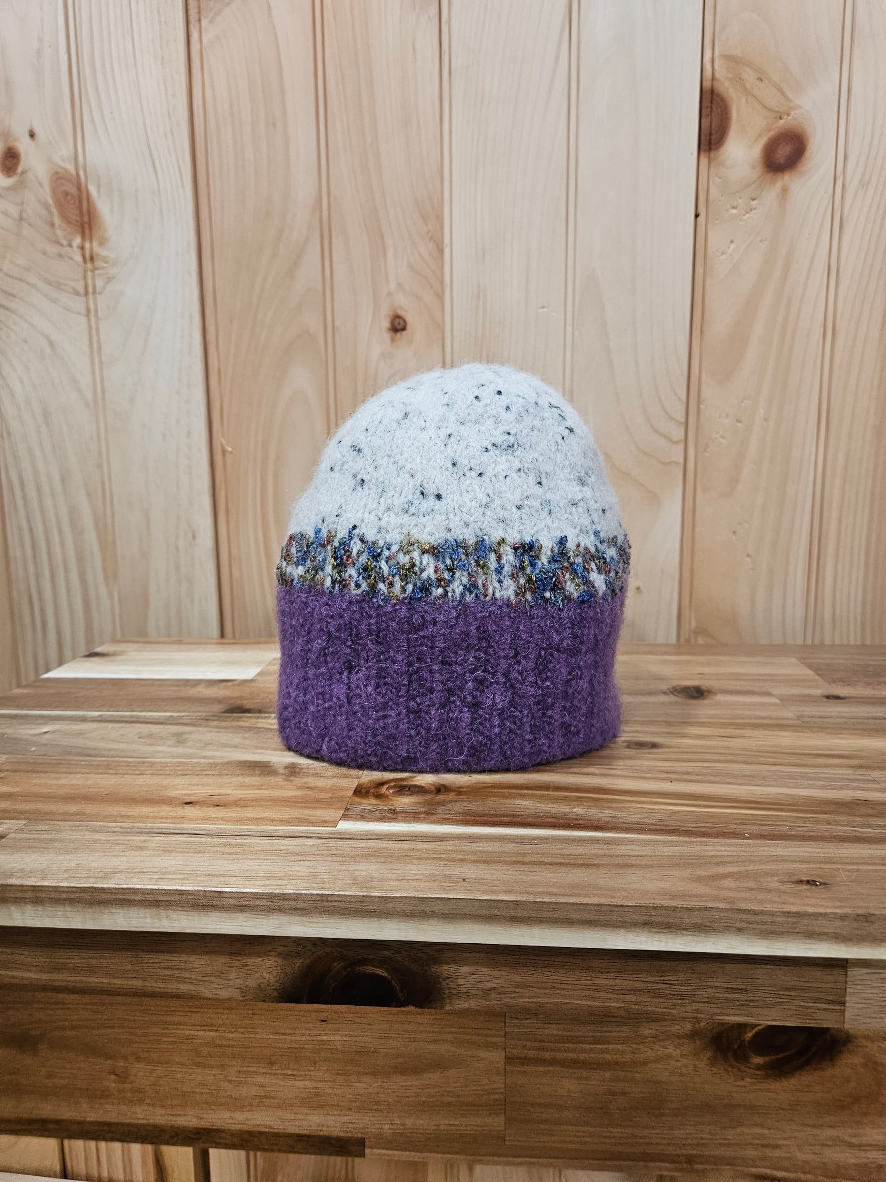 Hand-felted purple wool hat with a cream crown and a multicolored band, resting on a wood table.