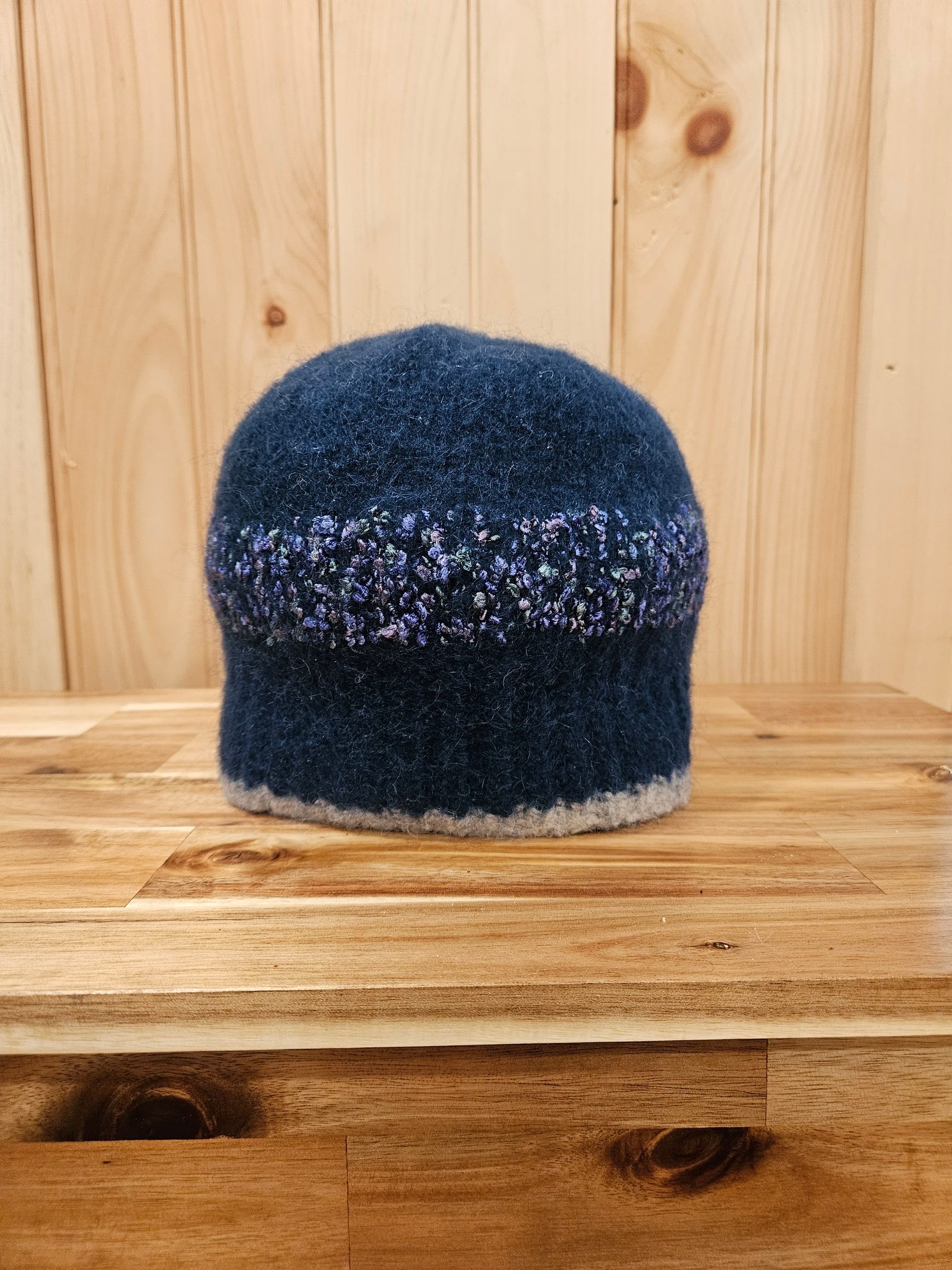 Navy blue felted wool hat with a dark speckled band and a pale gray rim, on a wood table.