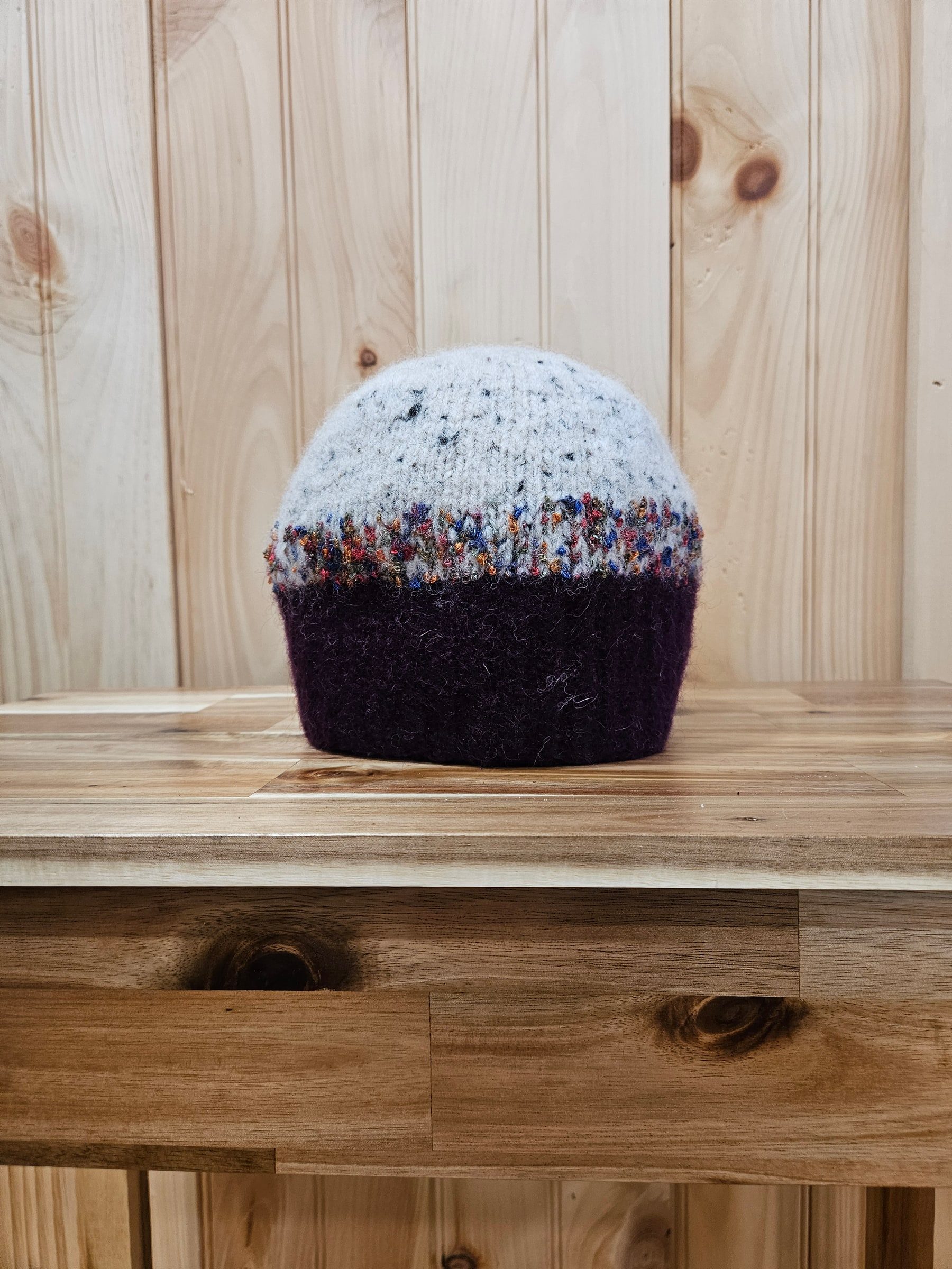 Burgundy and cream felted wool hat with a multicolored band, on a wood table.