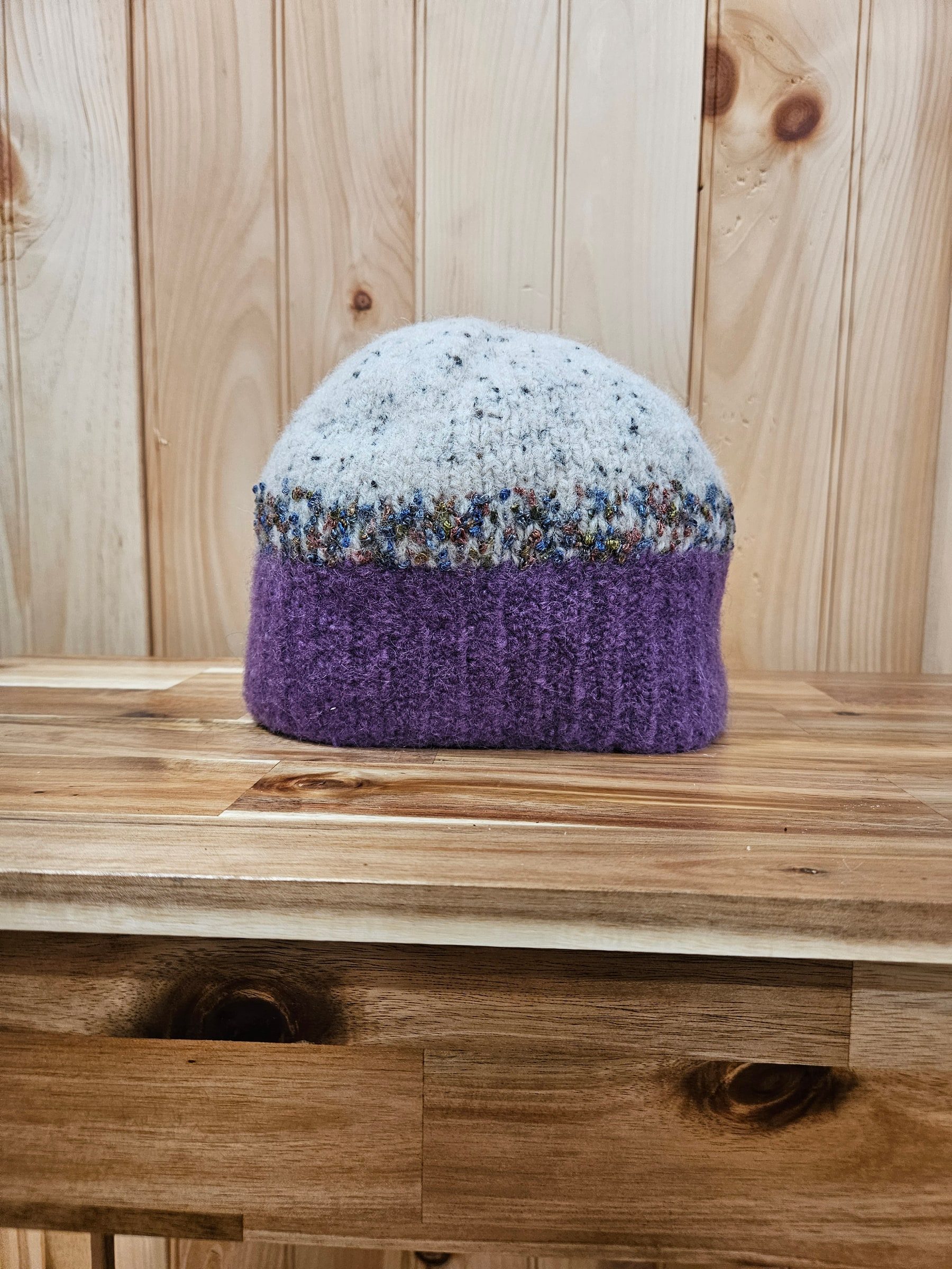 Purple and cream felted wool hat with a blue and rust band, on a wood table.